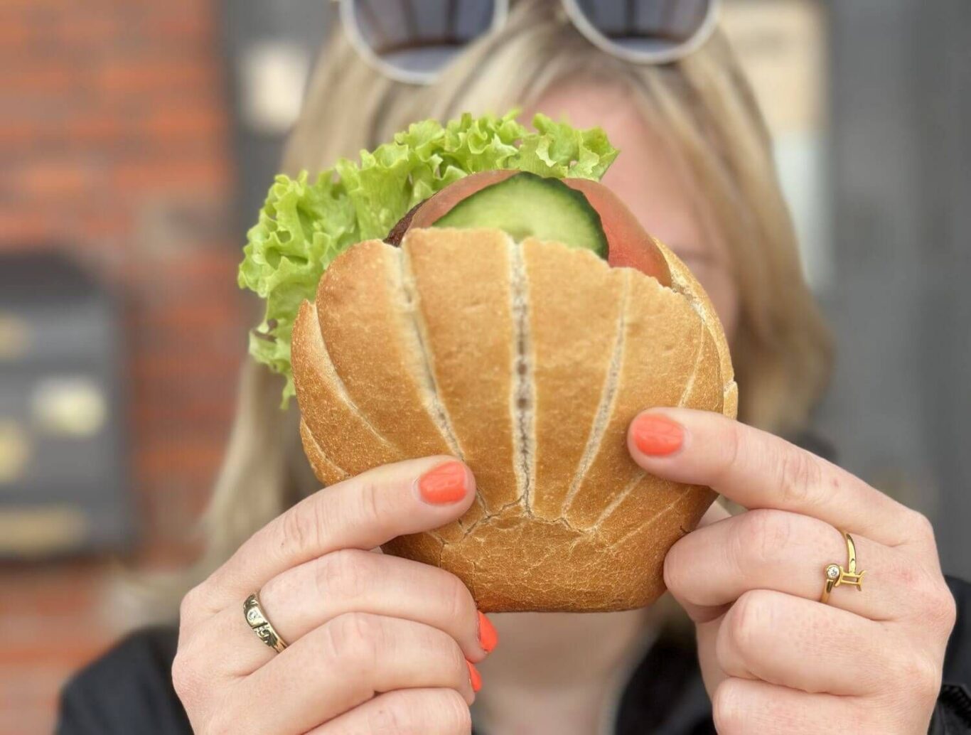 Eine Frau hält sich ein Fischbrötchen im Muschelform vor das Gesicht