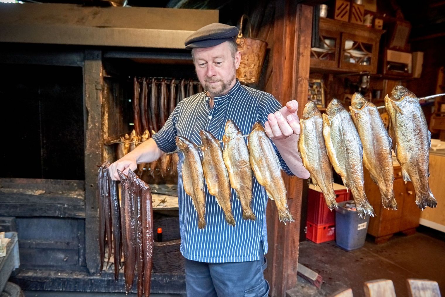 Ein Mann, maritim gekleidet, hält eine Stange mit geräucherten Fischen in der Hand