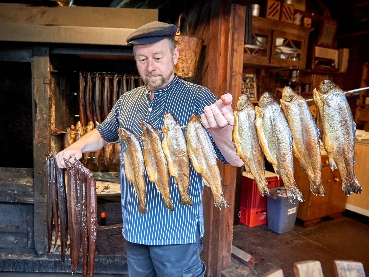 Ein Mann, maritim gekleidet, hält eine Stange mit geräucherten Fischen in der Hand