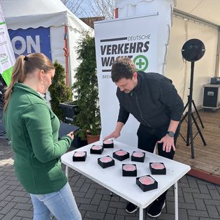 Eine Frau und ein Mann stehen an einem Tisch mit neun rot leuchtenden, sechseckigen Reaktionstestern. Im Hintergrund ist ein Roll-up-Banner der Deutschen Verkehrswacht Bremerhaven zu sehen.