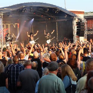 Eine Band spielt auf einer Musikbühne mit Publikum davor.