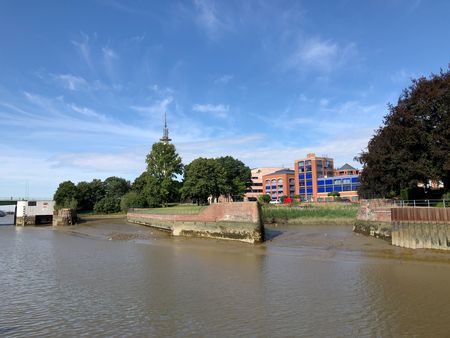 Das historische Wencke-Dock in Bremerhaven bei Ebbe, umgeben von Bäumen und modernen Gebäuden.