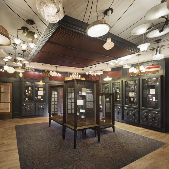 Ausstellungsraum mit Vitrinen, historischen Dokumenten und vielfältigen Lampen an der Decke