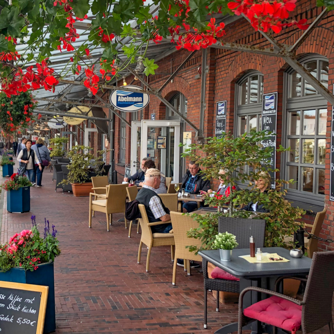 Menschen sitzen vor rotem Backsteingebäude im Schaufenster Fischereihafen Bremerhaven und genießen Speisen.
