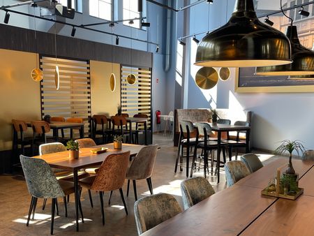Helles Restaurant mit modernen Holztischen, Polsterstühlen und großen goldfarbenen Lampen.