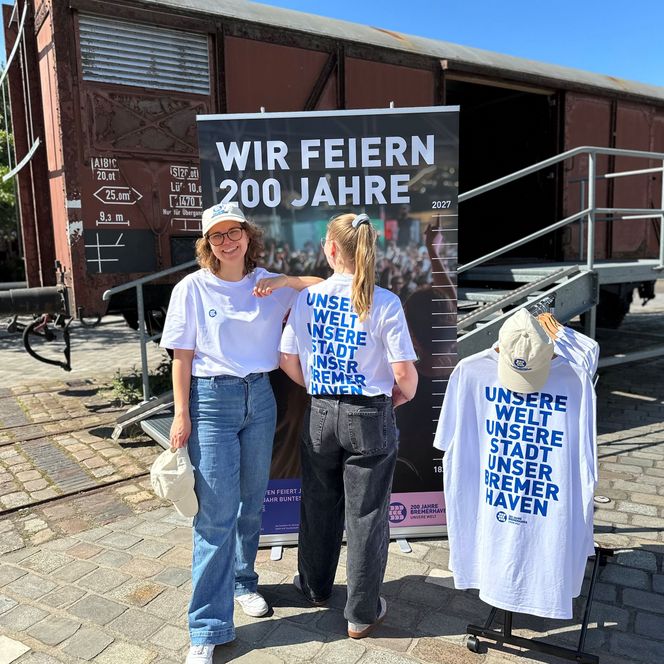 Zwei Frauen vor einem Banner mit der Aufschrift "Wir feiern 200 Jahre"