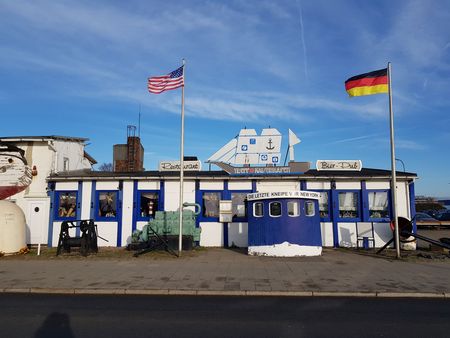 Treffpunkt Kaiserhafen mit maritimer Fassade, Flaggen und blauem Eingang.