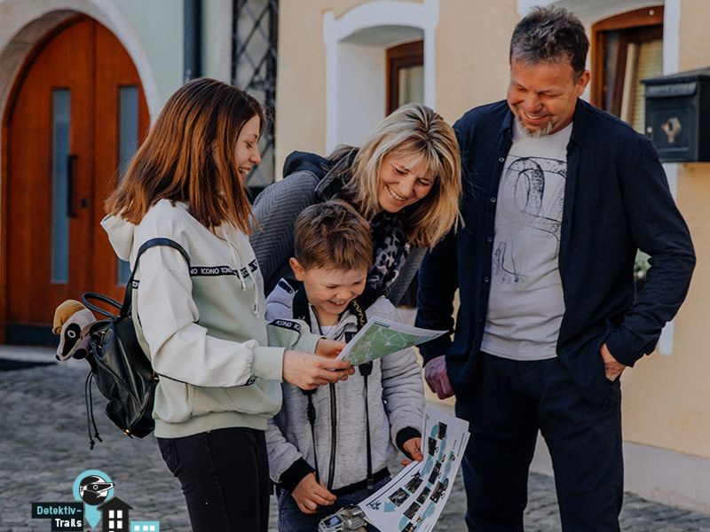 Eine lachende Familie betrachtet gemeinsam eine Karte auf dem Detektiv-Trail.