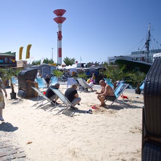 Im Sand im Schaufenster Fischereihafen sitzen und auf das Wasser schauen,