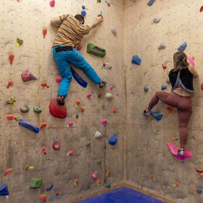 Zwei Personen klettern an einer bunten Boulderwand in der Kletterhalle Bremerhaven.