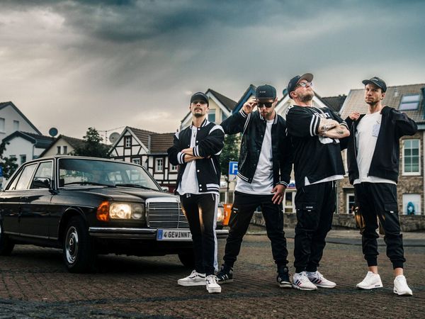 Vier Bandmitglieder vor einem Auto
