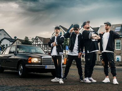 Vier Bandmitglieder vor einem Auto