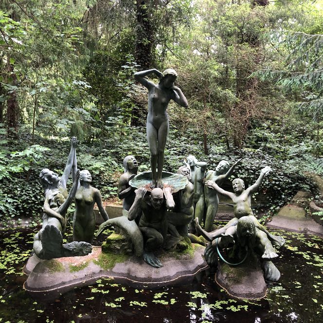 Bronzeskulpturengruppe "Die Geburt der Venus" mit neun Figuren in einem Teich, umgeben von dichtem grünen Wald.