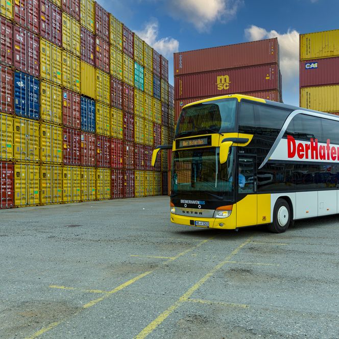 Ein gelb-weißer Doppelstockbus steht vor bunten, gestapelten Containern im Hafen.