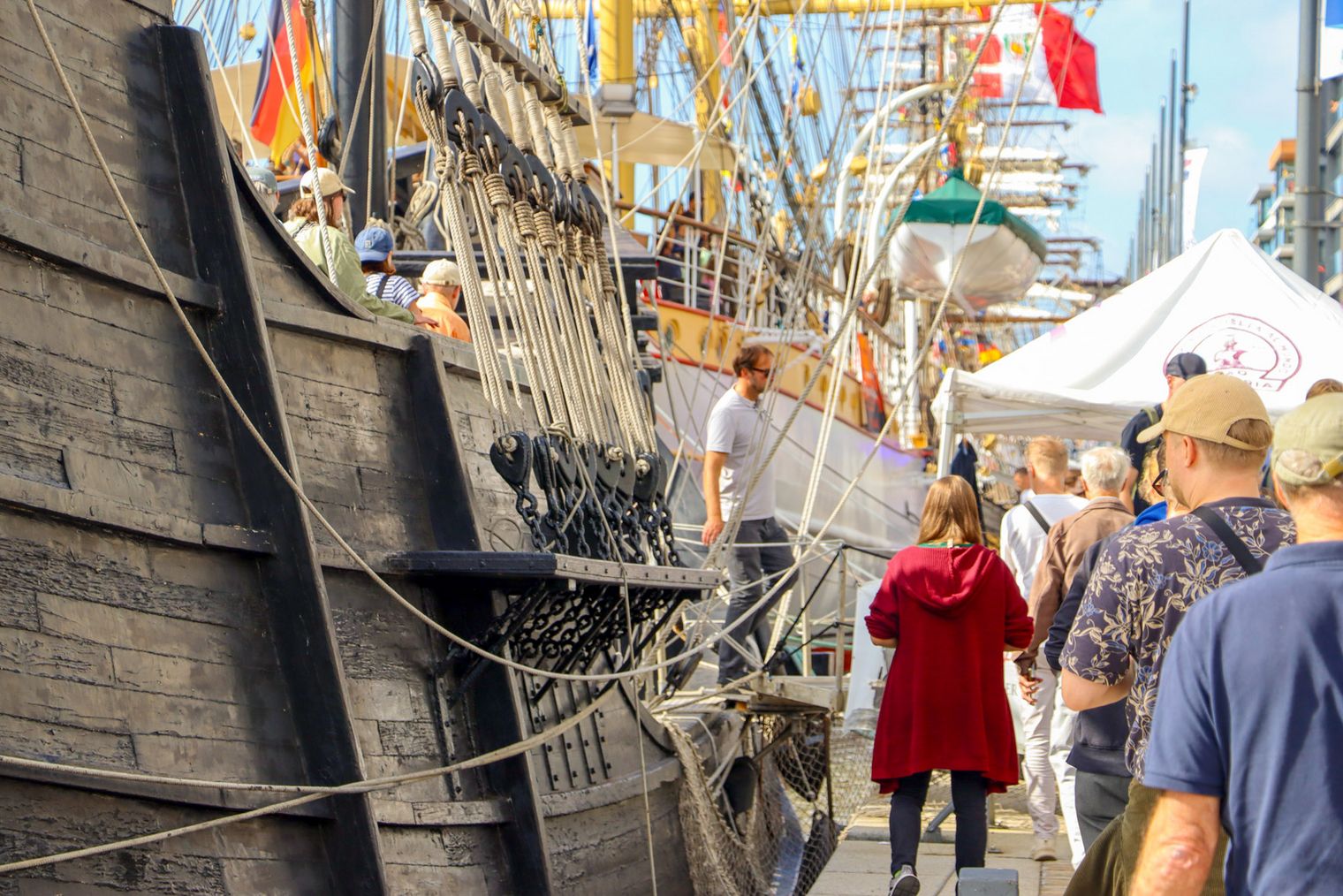 Menschen schlendern an der Kaje entlang, an der wunderschöne Segelschiffe liegen