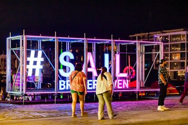 Leuchtende #SAIL Bremerhaven-Installation bei Nacht, umgeben von Besucherinnen und Besuchern.