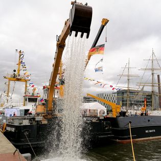 Der Bagger an Bord der Franzius Plate entlädt seine große Schaufel ins Hafenbecken