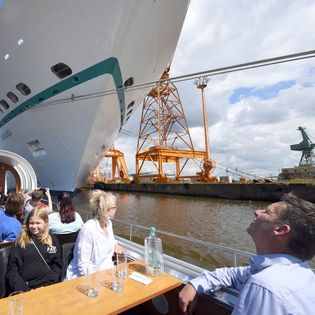 Familie auf einer Barkasse mit geöffnetem Glasdach blickt zu einem Kreuzfahrtschiff empor