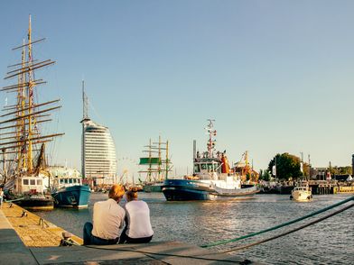 Ein Pärchen sitzt in Bremerhaven am Hafenbecken und schaut auf die vorbeifahrenden Schiffe