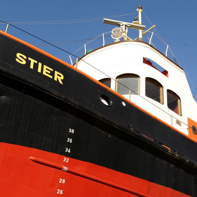 Schlepper „Stier“ mit rot-schwarzem Rumpf und weißen Aufbauten vor blauem Himmel im Museumshafen.