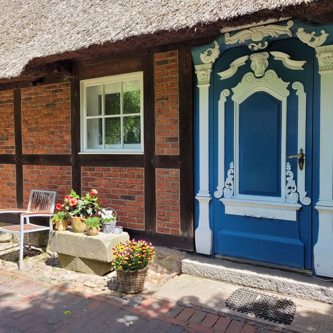 Historisches Reetdachhaus mit aufwendig verzierter blauer Eingangstür und Ziegelfassade.