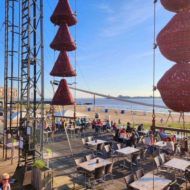 Belebte Außenterrasse am Strandcafé Seelust mit roten Deko-Körben, Sandstrand und Wasser.