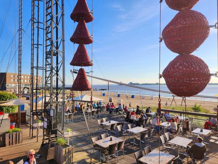 Belebte Außenterrasse am Strandcafé Seelust mit roten Deko-Körben, Sandstrand und Wasser.