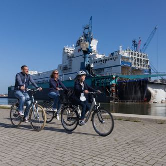 Familie auf Rädern fährt durch den Hafen an einem großen Schiff vorbei