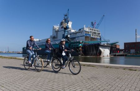 Familie auf Rädern fährt durch den Hafen an einem großen Schiff vorbei