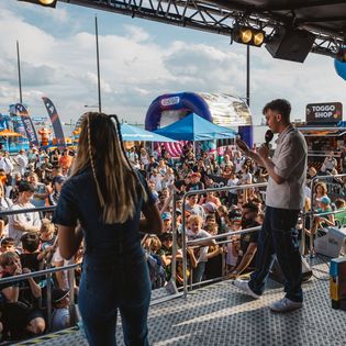 Zwei Moderatoren sprechen von einer Bühne aus ins Publikum