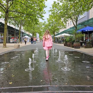 Ein Mädchen springt durch die Wasserfontainen in der Fußgängerzone.