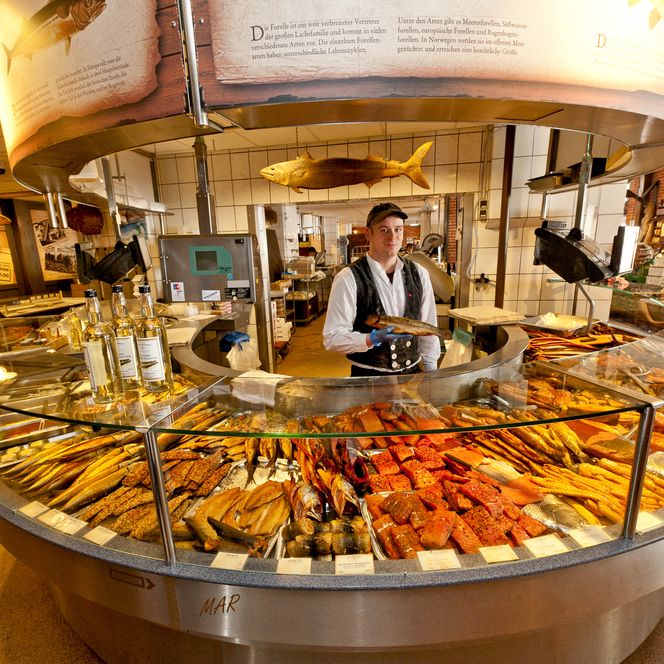 Verkäufer hinter runder Theke mit großer Auswahl an frisch geräuchertem Fisch in Bremerhaven