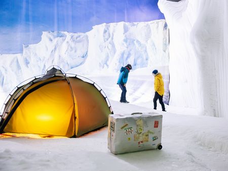 Zwei Kinder in Winterkleidung erkunden eine Eislandschaft mit beleuchtetem Zelt und Koffer im Klimahaus Bremerhaven