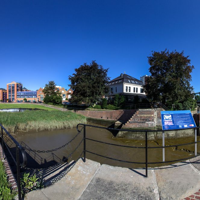 Historisches Wencke-Dock in Bremerhaven bei Sonnenschein, umgeben von Wasser, Bäumen und Häusern.