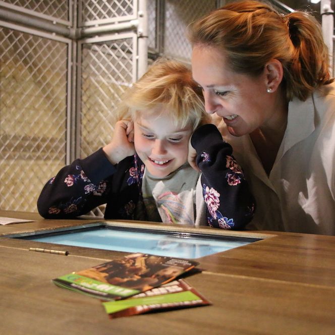 Eine Frau und ein Kind betrachten lächelnd eine interaktive Ausstellung im Deutschen Auswandererhaus.