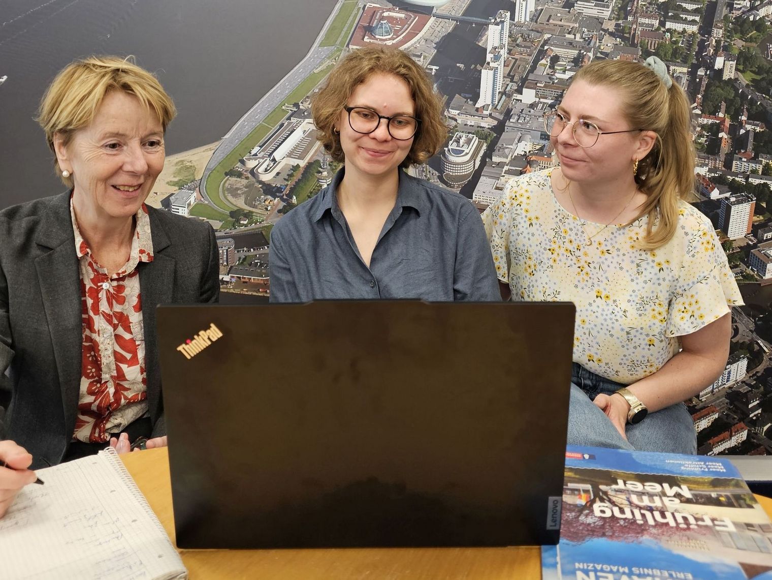 Drei Frauen sitzen an einem Schreibtisch und schauen auf einen Bildschirm