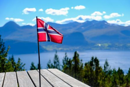 Eine norwegische Flaggen steht auf einem Steg an einem See. Im Hintergund Berge