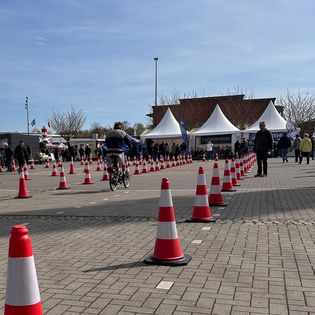 Fahrrad-Testparcours mit rot-weißen Pylonen auf einem Messeplatz; ein Radfahrer durchfährt den Slalomkurs, im Hintergrund Pagodenzelte und Besucher.