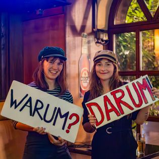 Zwei Frauen mit einem Schild "Warum?" und "Darum"