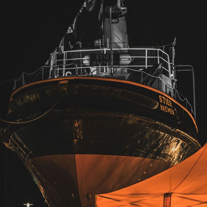 Bugsierschiff „Stier“ im Hafen Bremerhaven, nachts stimmungsvoll angestrahlt vor dunklem Himmel