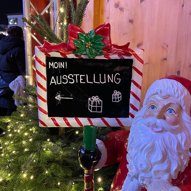 Weihnachtsmann mit Schild "Zur Ausstellung"