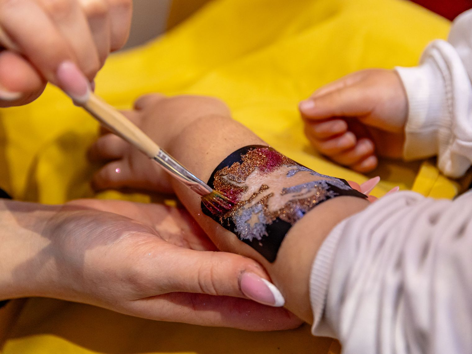Eine Kinderhand wird mit Glitzer-Tattoos bemalt