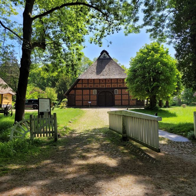 Historisches Fachwerkhaus mit Reetdach, großer Einfahrtstür und umgeben von Bäumen.