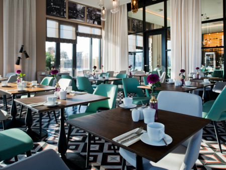 Helles Restaurant mit gedeckten Holztischen, türkisen Stühlen und geometrischem Fliesenboden.