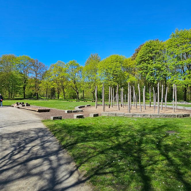Spaziergänger im Gesundheitspark Speckenbüttel neben einer Fitnessanlage mit Holzstangen.