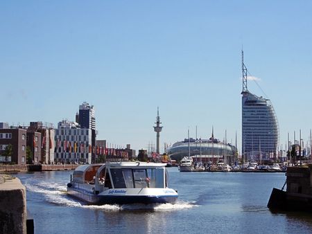 Ausflugsboot fährt durch den Hafen von Bremerhaven vor markanter Skyline bei blauem Himmel.