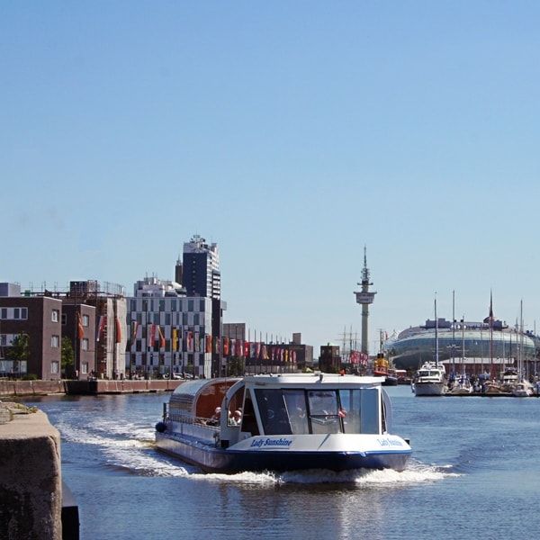 Ausflugsboot fährt durch den Hafen von Bremerhaven vor markanter Skyline bei blauem Himmel.