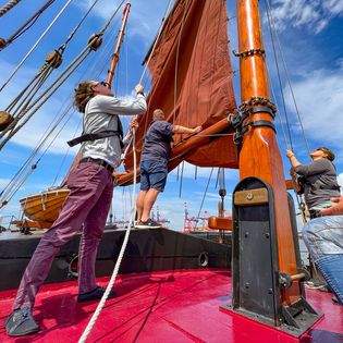 Ein Mann hilft beim Segel hissen auf der Adler von Krautsand
