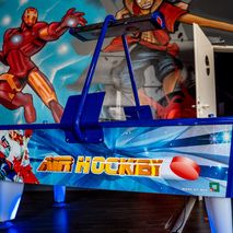 Blau beleuchteter Air-Hockey-Tisch vor einer Wandbemalung mit Iron Man und einer Manga-Figur.