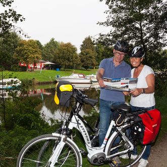 Ein Pärchen mit Fahrrädern am Straßenrand. Sie studieren eine Fahrradkarte.